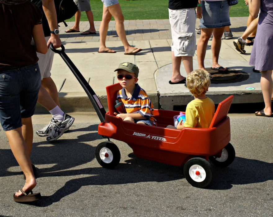Two children are being pulled in a red wagon by a parent