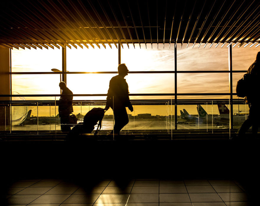 People walk through an airport with the sun shining behind them through the windows