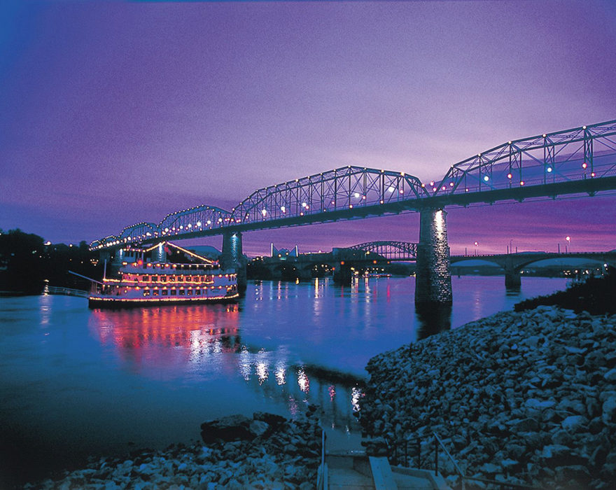 The sun sets over the river in Chattanooga, TN with a view of the purple sky behind the bridge